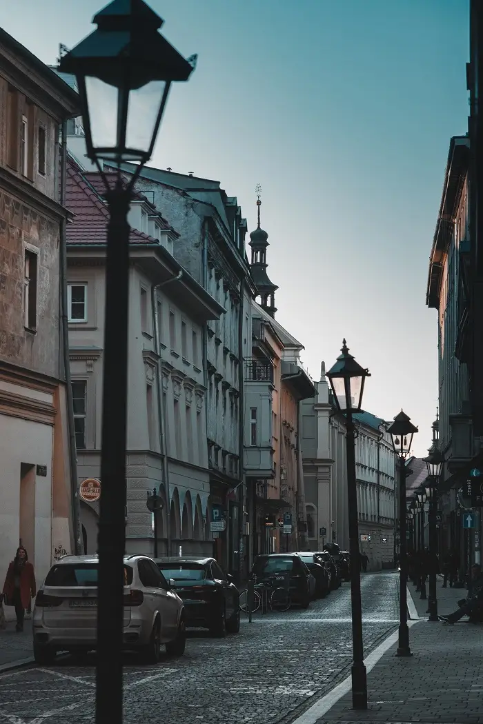 A street with buildings, lamp posts, and parked cars in Krakow