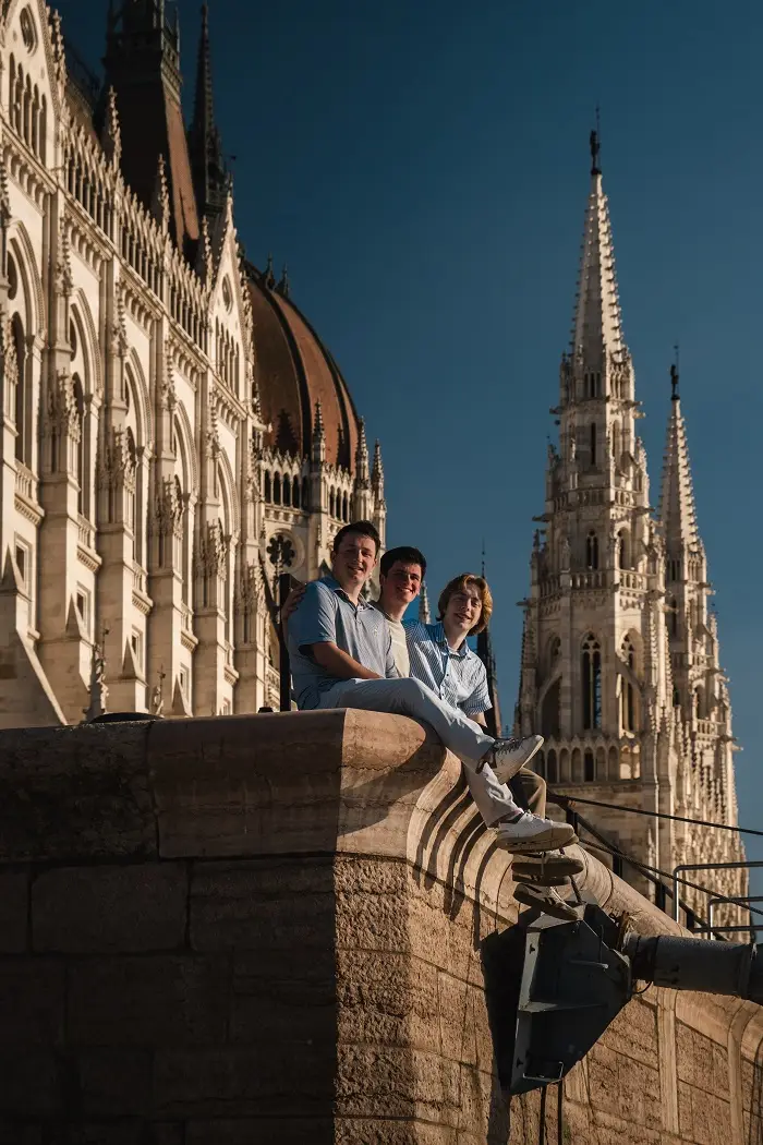 Three males sitting along the ledge in front of the Parliament building