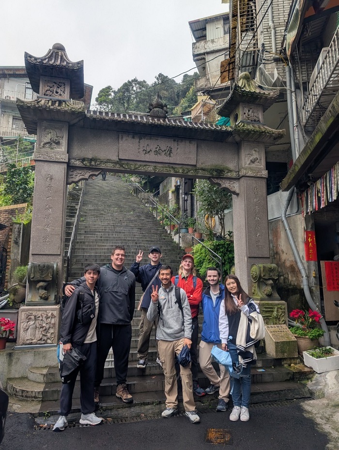 A group of CET Taiwan students and language partners smiling at the bottom of a staircase with a gate and Chinese inscriptions on the columns