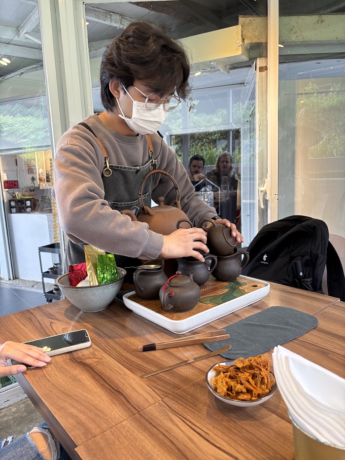 A person wearing a mask while pouring tea on a tea set