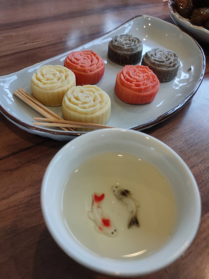 Six little tea snacks that are shaped like roses next to a little dish with two koi fish design on it