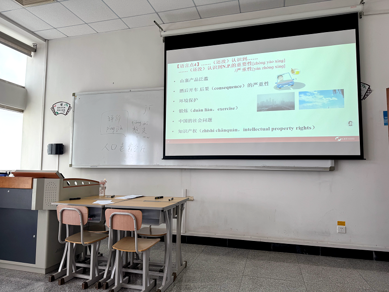 A classroom with an empty chair and desk with a PowerPoint on a screen with Chinese and English words