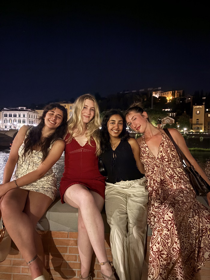 Four CET Florence female students smiling while sitting on a ledge by the Arno River at night