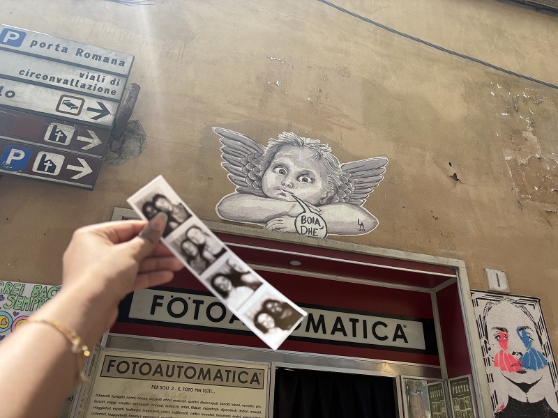 A hand holding a strip of film photos from a photo booth on a street in Florence, Italy