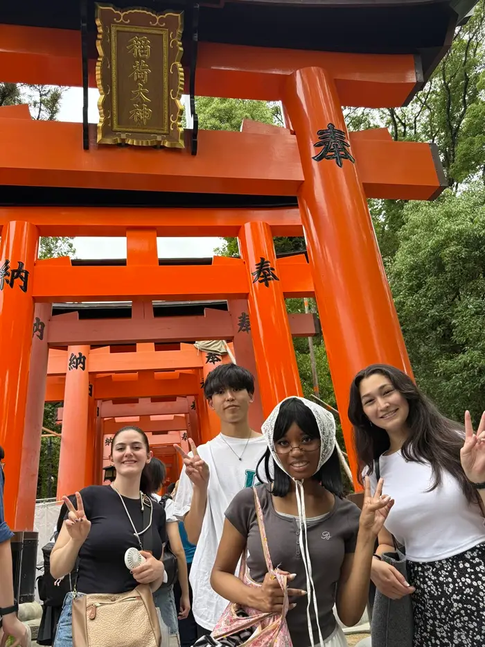 A group of four CET Japan students smiling and posing under a torii gate at Fushimi Inari in Kyoto, Japan