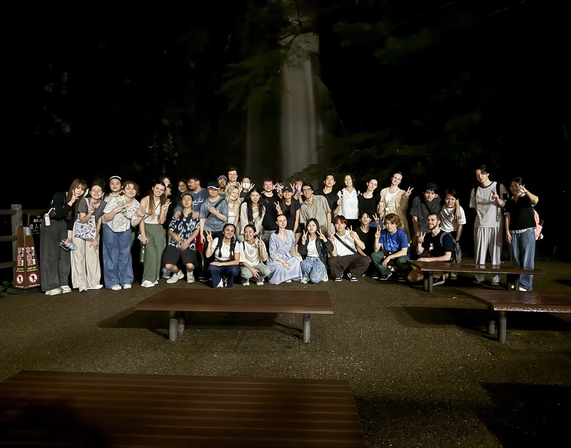 A large group photo of CET Japans students and local Japanese students near Minoh Waterfalls at night by wooden benches