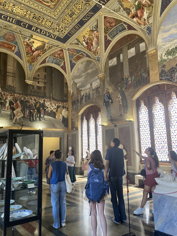 People looking up at a series of intricately frescoed rooms in Palazzo Publico