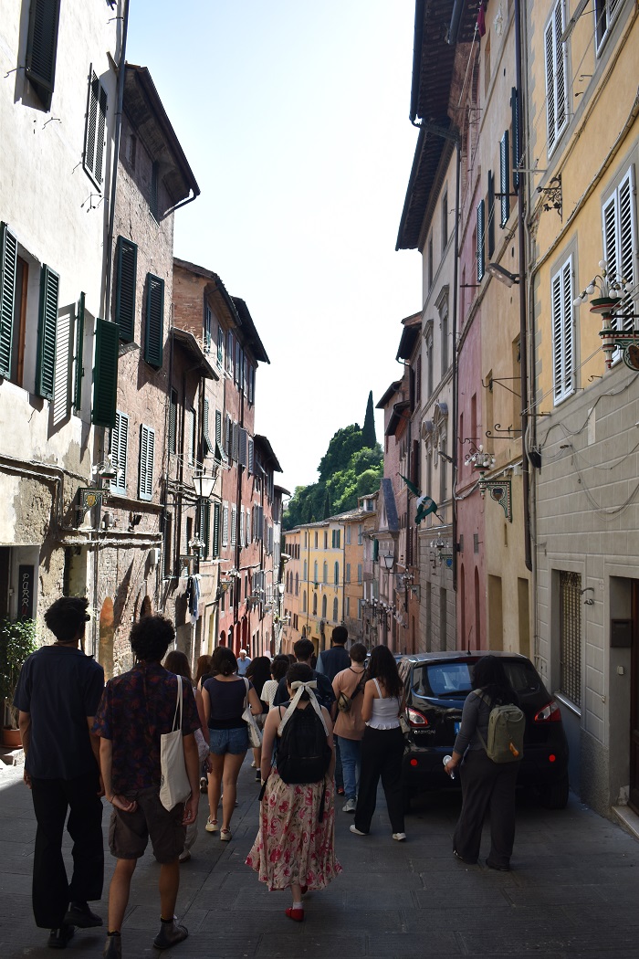 A narrow street in Siena, Italy of building on each side and a group of CET Siena students walking down the middle