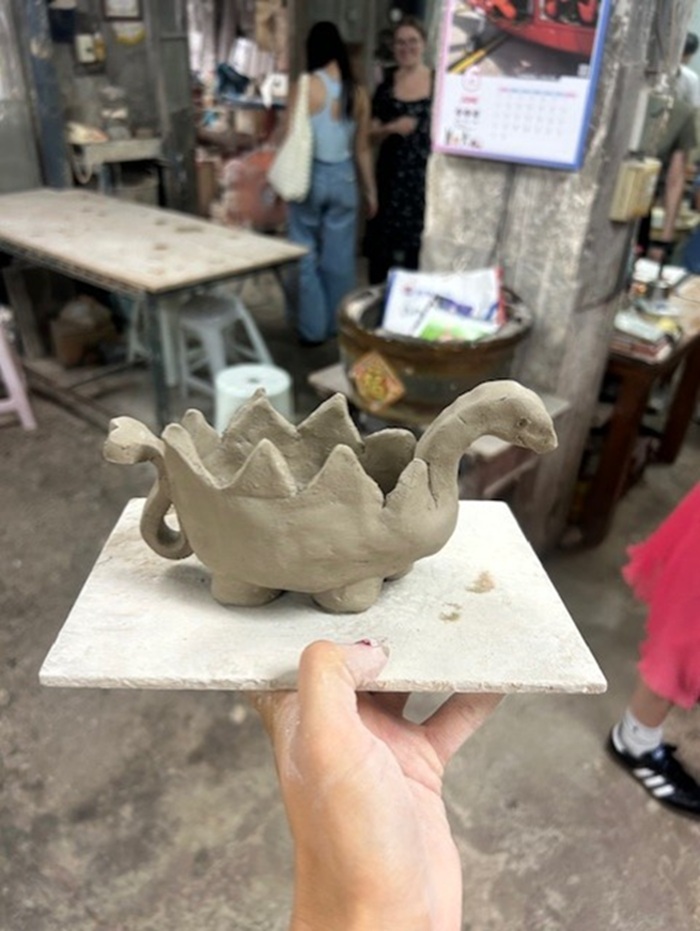 A hand holding up a pottery of a dinosaur