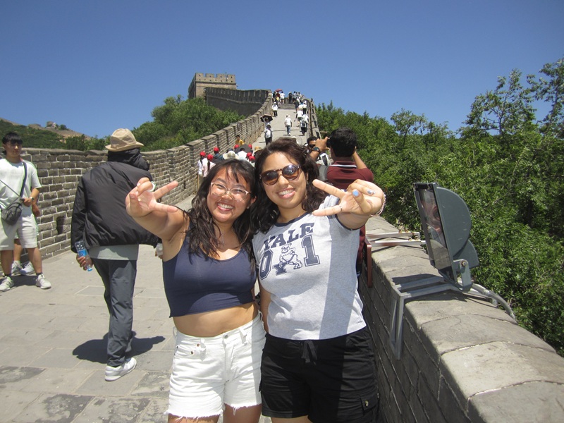 Two female CET Beijing students holding up peace signs and smiling while hiking back up the Great Wall in China