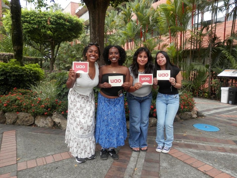 A group of four CET Colombia students holding up signs that said "uao" on it while standing on the campus of Universidad Autónoma de Occidente
