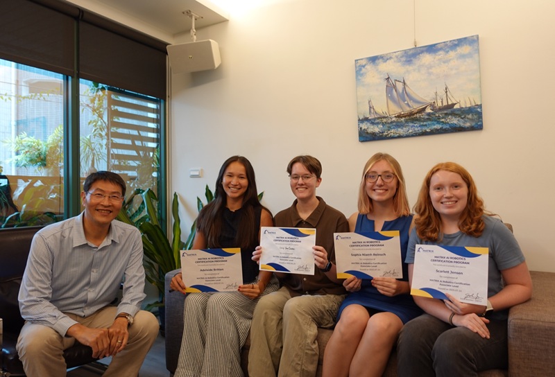 A group of four students holding up a certificate paper for their internship with their advisor sitting to the left of them