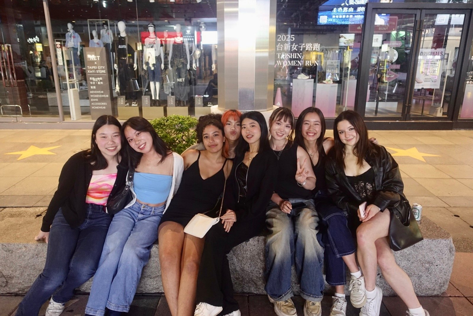A group of eight females sitting on a rock-bench outside at night in XinYin