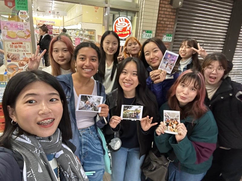 A group photo of CET Taiwan students and local roommates holding up printed postcards while standing in front of a 7-Eleven