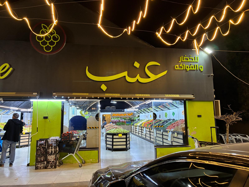 A view of the Inab market in Jordan with large Arabic words outside the building and isles of fresh produce within the store