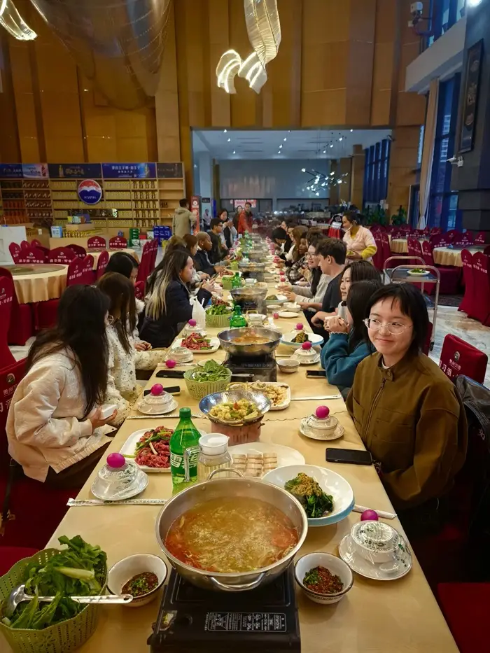 A rectangular Miao long-table feast featuring sour soup beef and stir-fried dishes and people sitting around it
