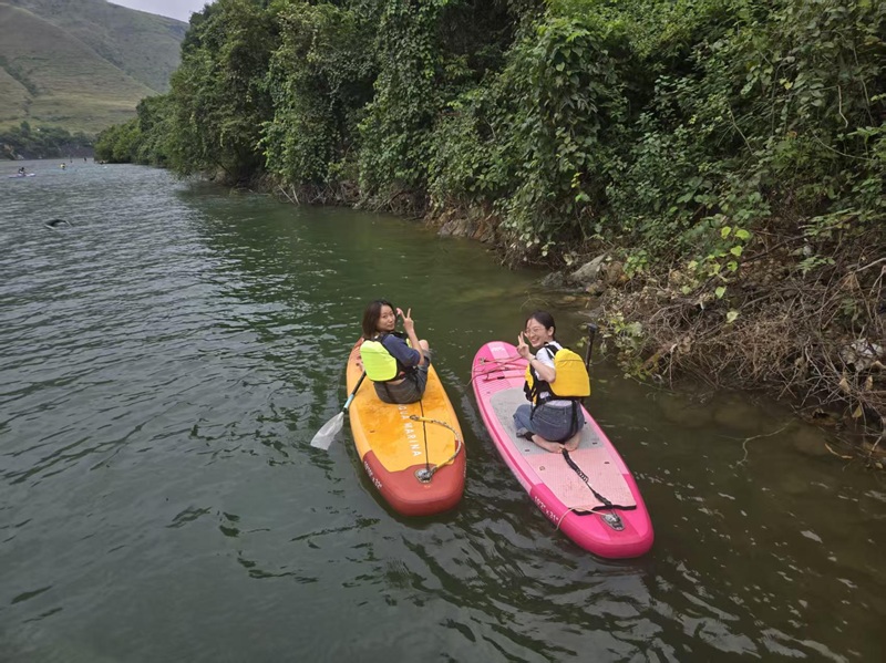 Two CET Shanghai students smiling and holding up peace signs while paddleboating