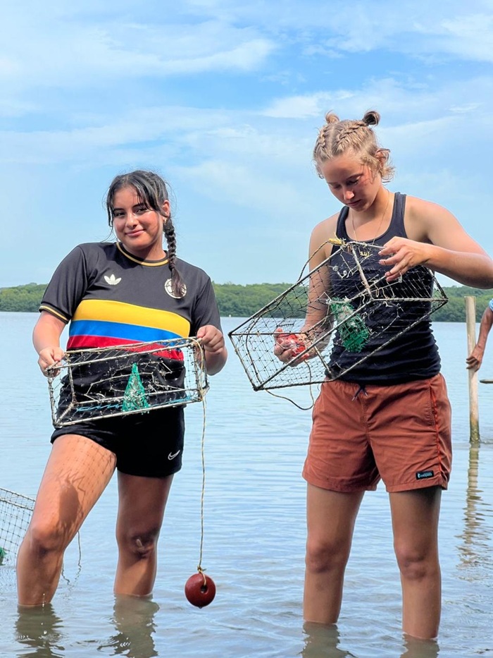 Two CET Colombia students holding crab nets while standing in the water