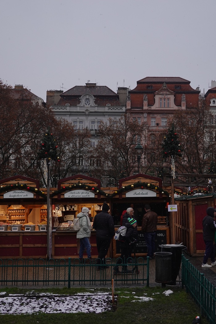 People walking along Christmas stalls at an outdoor market in Prague on a cloudy day