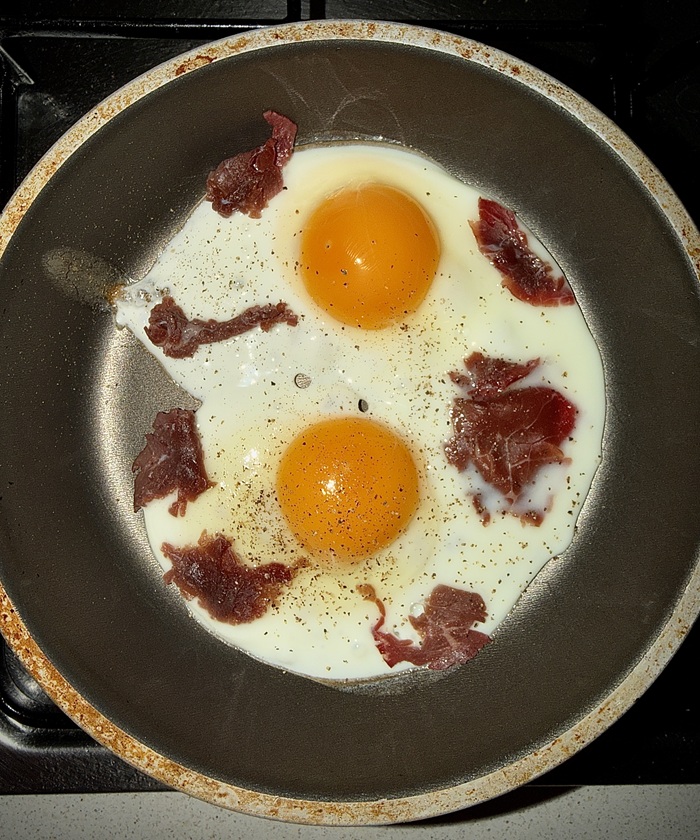 A pan with two fried eggs and bits of meat ripped on top