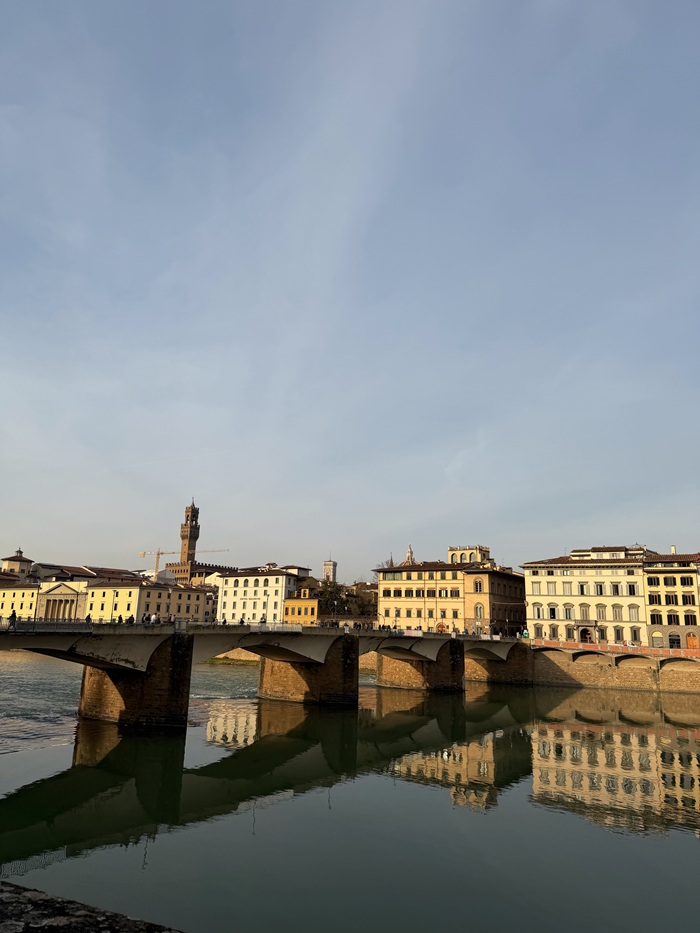 A busy bridge with people crossing it over the Arno River in Florence, Italy on a clear, cloudless day
