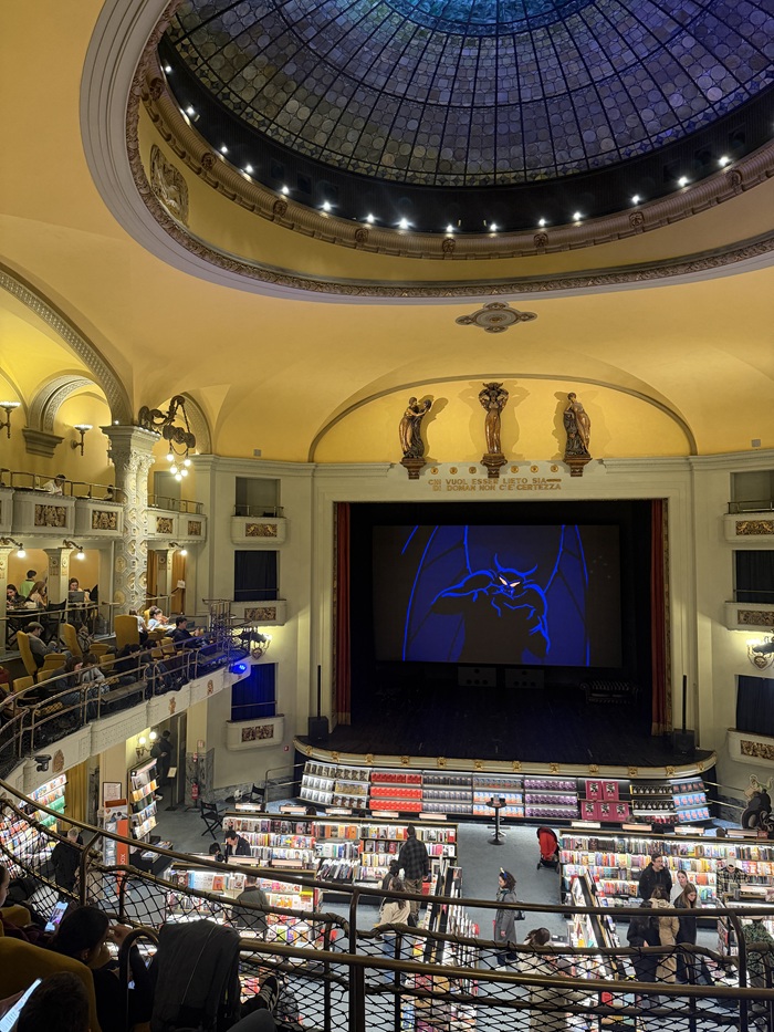 The inside of the Giunti Odeon, which is filled with movie-like seats, books, all in front of a large screen playing a movie in Florence, Italy