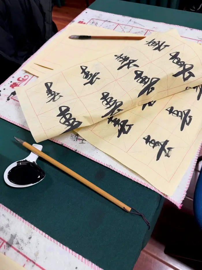 Ink, calligraphy pen, and sheets of paper with calligraph practice on them in Chinese characters