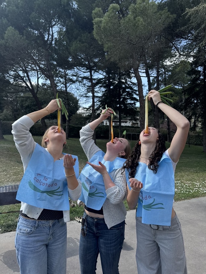 Three CET Barcelona students wearing bibs and eating calcotadas, long green onions dipped in sauce