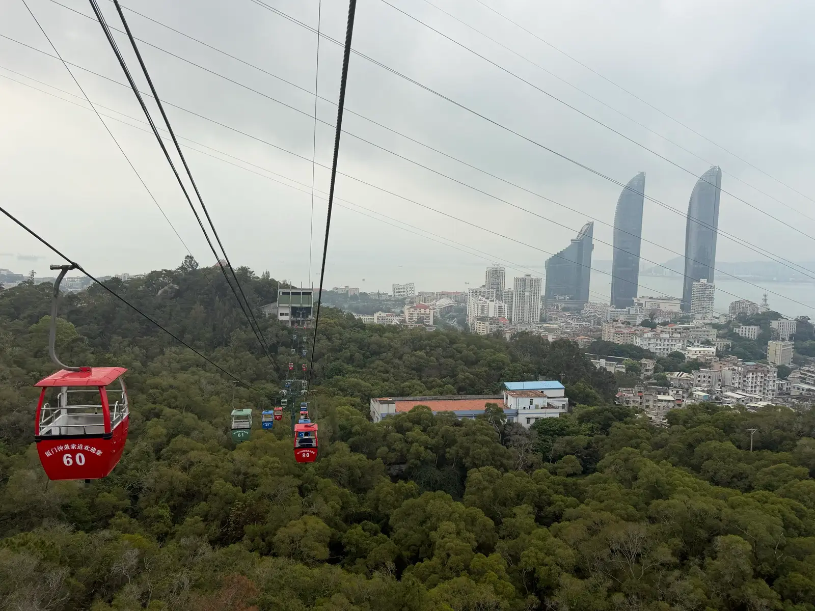 The view from a cable car in Xiamen overlooking a large portion of greenery and in the distance, the ocean.
