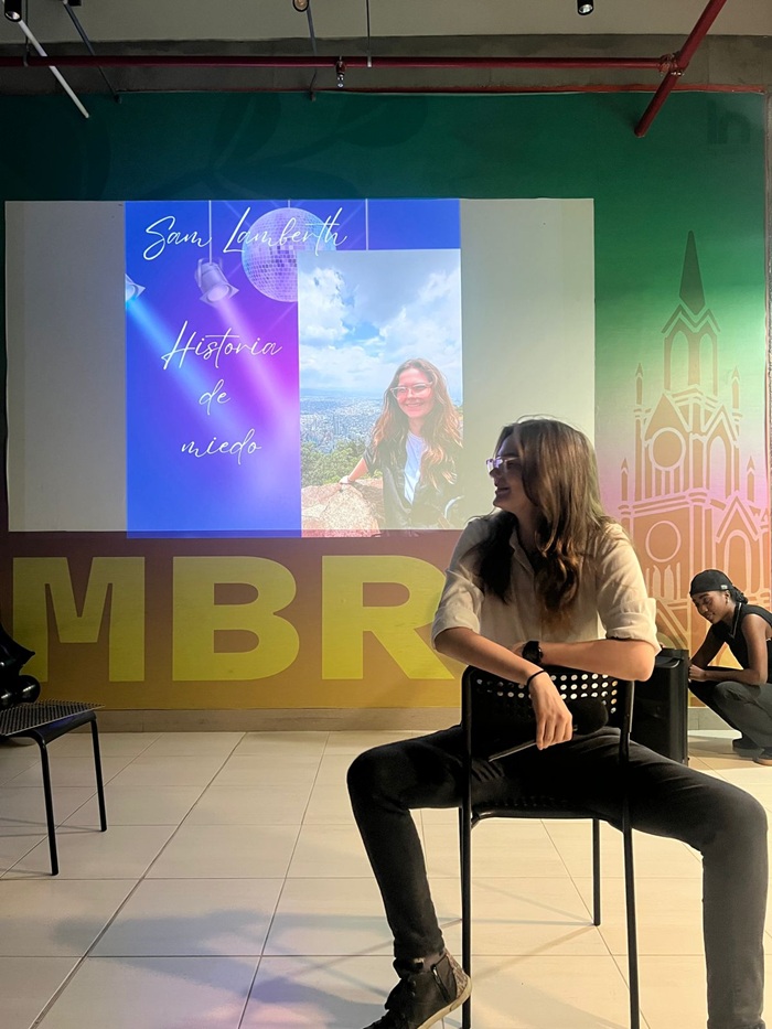 A student sitting in a chair while presenting in front of a screen projector
