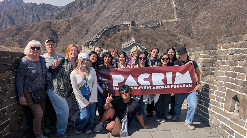 A group of students holding a banner that says "PACRIM Pacific Rim Study Abroad Program" while standing at the Great Wall of China