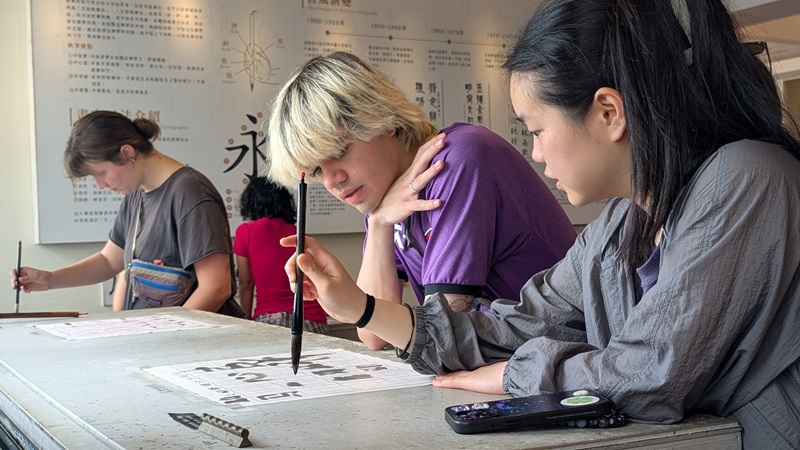 Three students practicing Chinese character calligraphy with a paintbrush