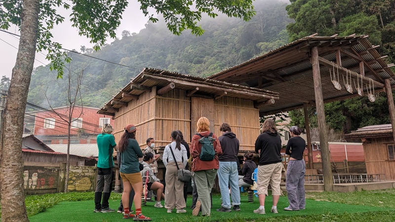 A group of students getting a tour of a local Tayal community school and seeing a traditional grainery and house