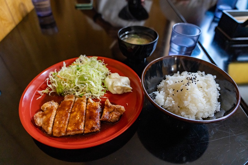 A dish of Tonkatsu, a Japanese deep-fried pork cutlet, which is breaded in panko besides a bowl of rice, soup, and a cup of water.