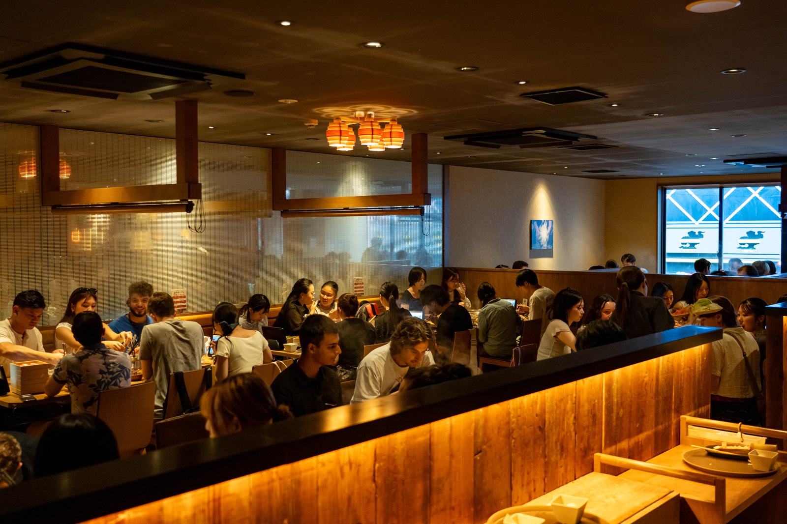 The interior of a Japanese Izakaya restaurant with wooden booths and warm lighting.