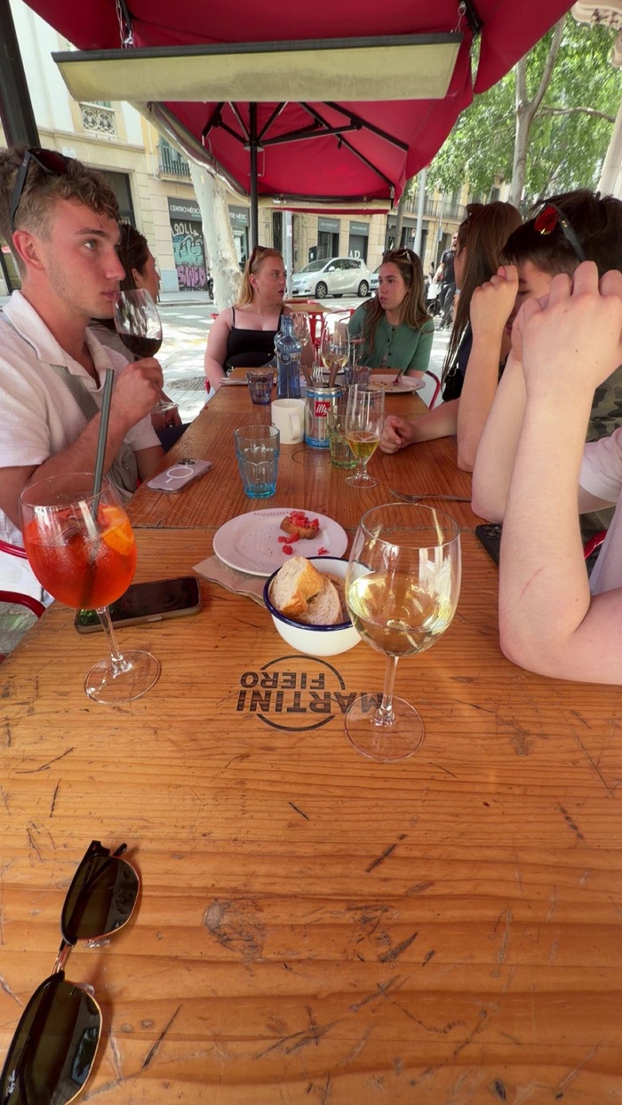 A group of students sitting together around a rectangular wooden table with drinks and appetizers in the middle