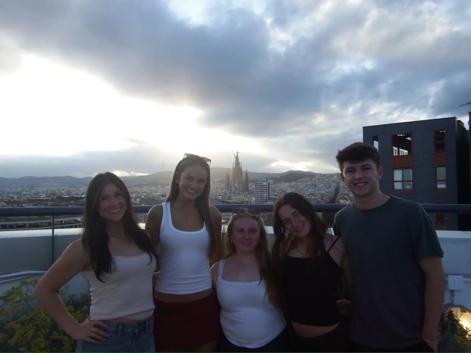 A group of CET Barcelona students smiling while on a rooftop with views of Barcelona city and the Sagrada Familia in the distance