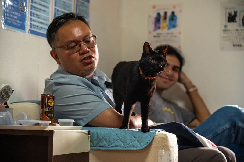 A CET Japan staff sitting on a sofa with a black cat standing on their lap.