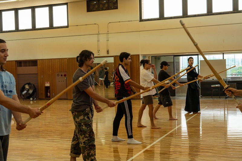 CET Japan students in a kendo training session holding shinai (bamboo swords) to practice, which is held inside a wooden-floored gymnasium.