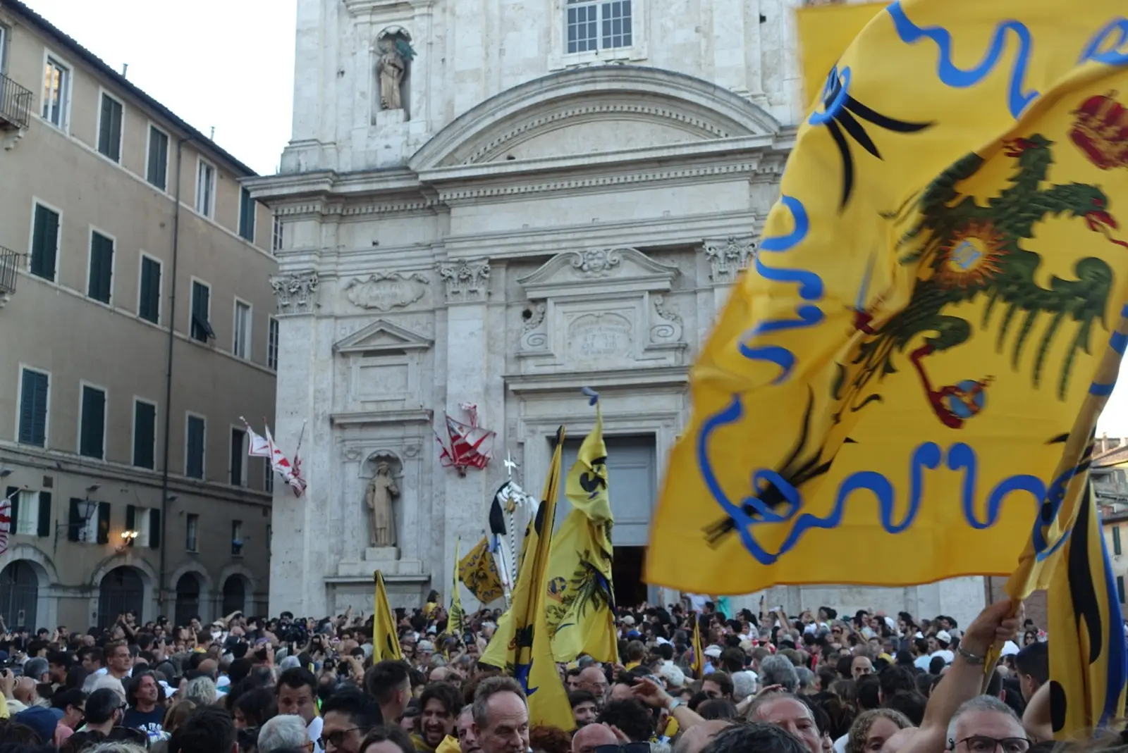 A large crowd with flags by the Collegiata di Santa Maria di Provenzano in Siena, Italy