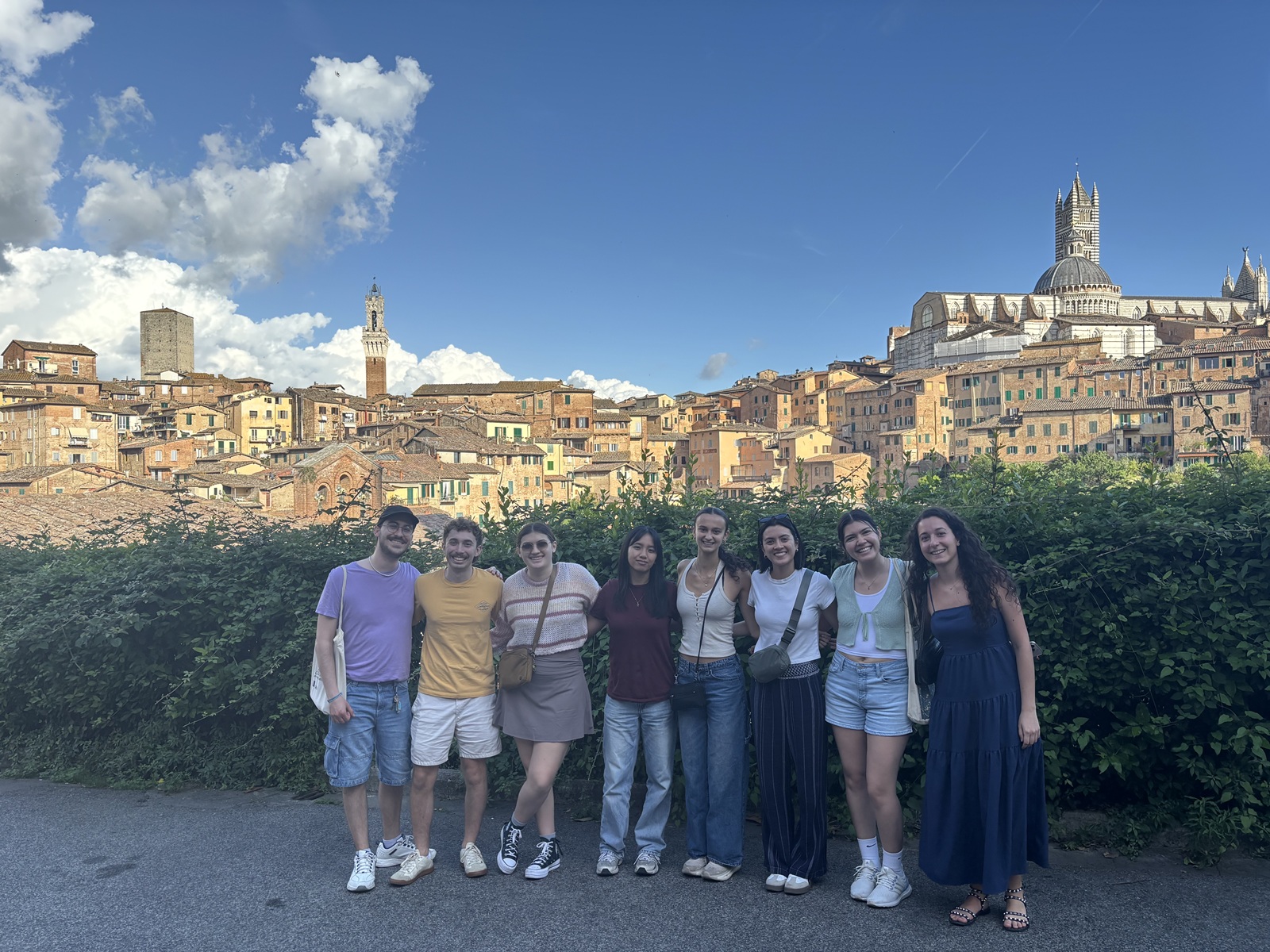 A group of CET Siena students and their local roommates standing in front of the skyline of Siena, Italy.