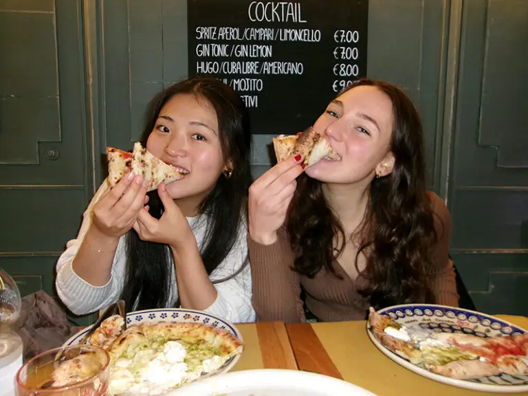 students biting into a slice of pizza