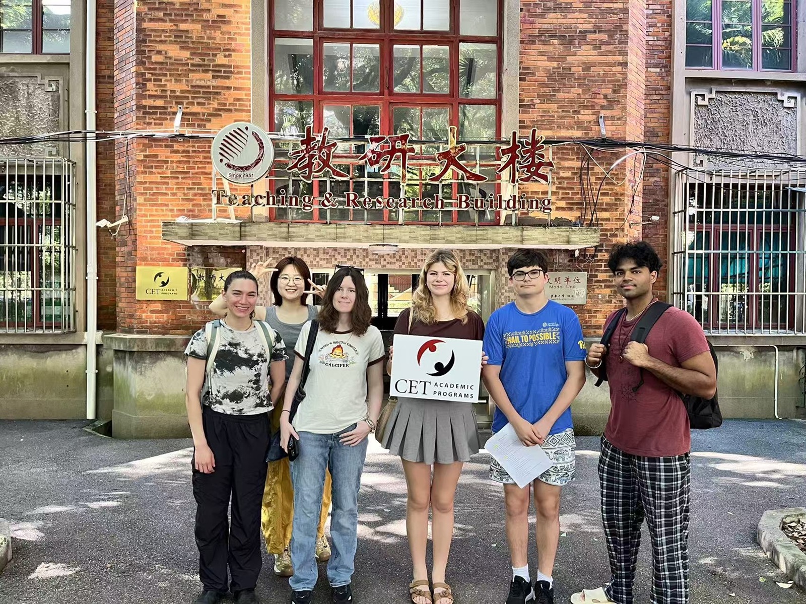 A group of CET Shanghai students smiling in front of a building that says "Teaching & Research Building" in China