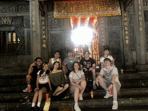 A group of CET Taiwan students and their local roommates and language partners sitting on the stone steps of Longshan Temple in Taipei, Taiwan