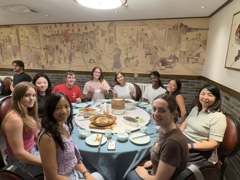 A group photo of CET Beijing students and staff sitting around a round table with food inside of a restaurant.