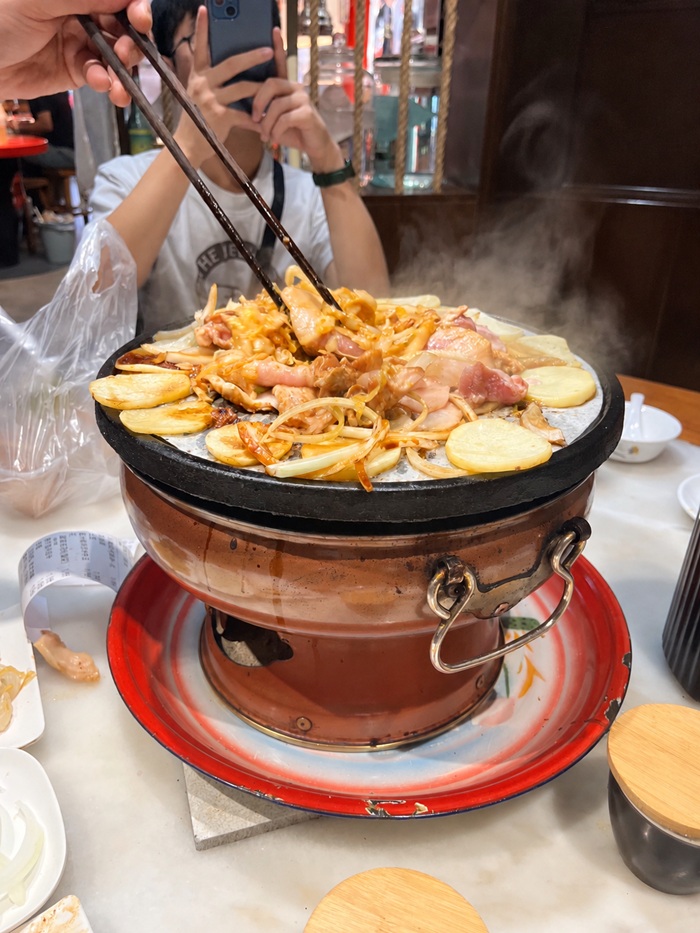 Chopsticks holding a piece of meat over a hot stone.