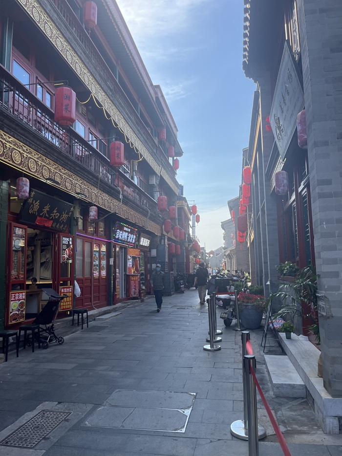 A hutong street in Beijing lined with vendors, snack and gift shops, and local businesses.