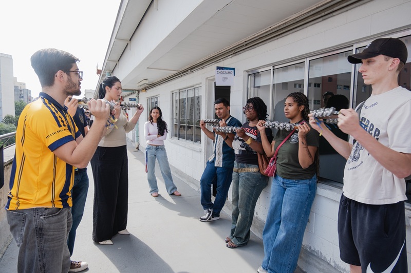CET students and local students from Pontifícia Universidade Católica de São Paulo playing the chocalho together while outside of a buillding