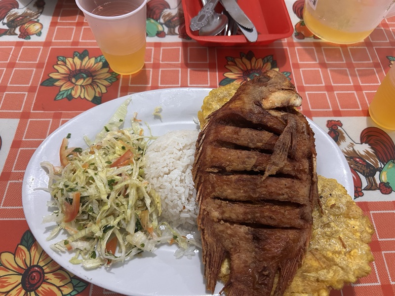 A plate with vegetables, rice, and a fried fish.