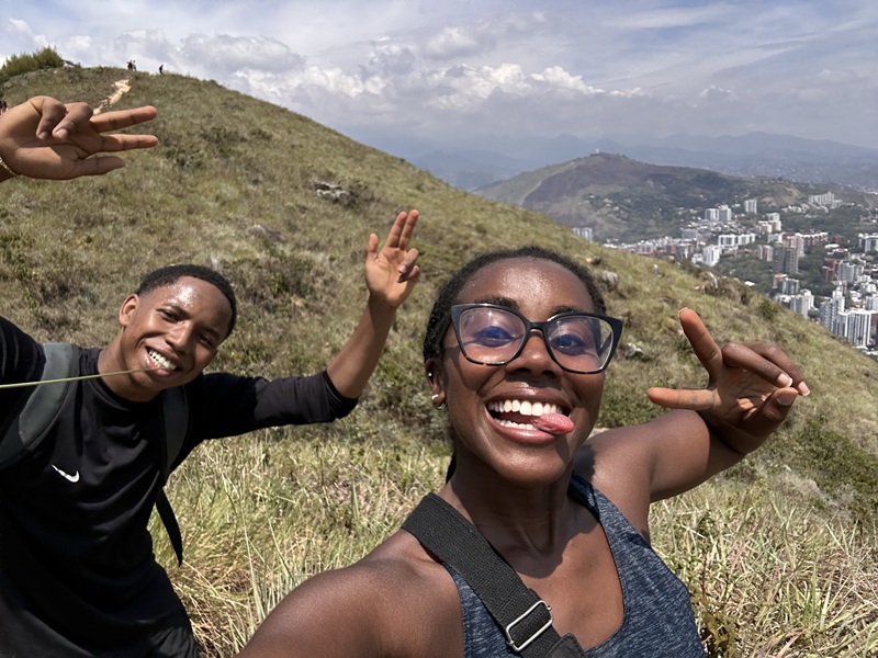A CET Colombia student and a local roommate posing while hiking with views of a city in the background.